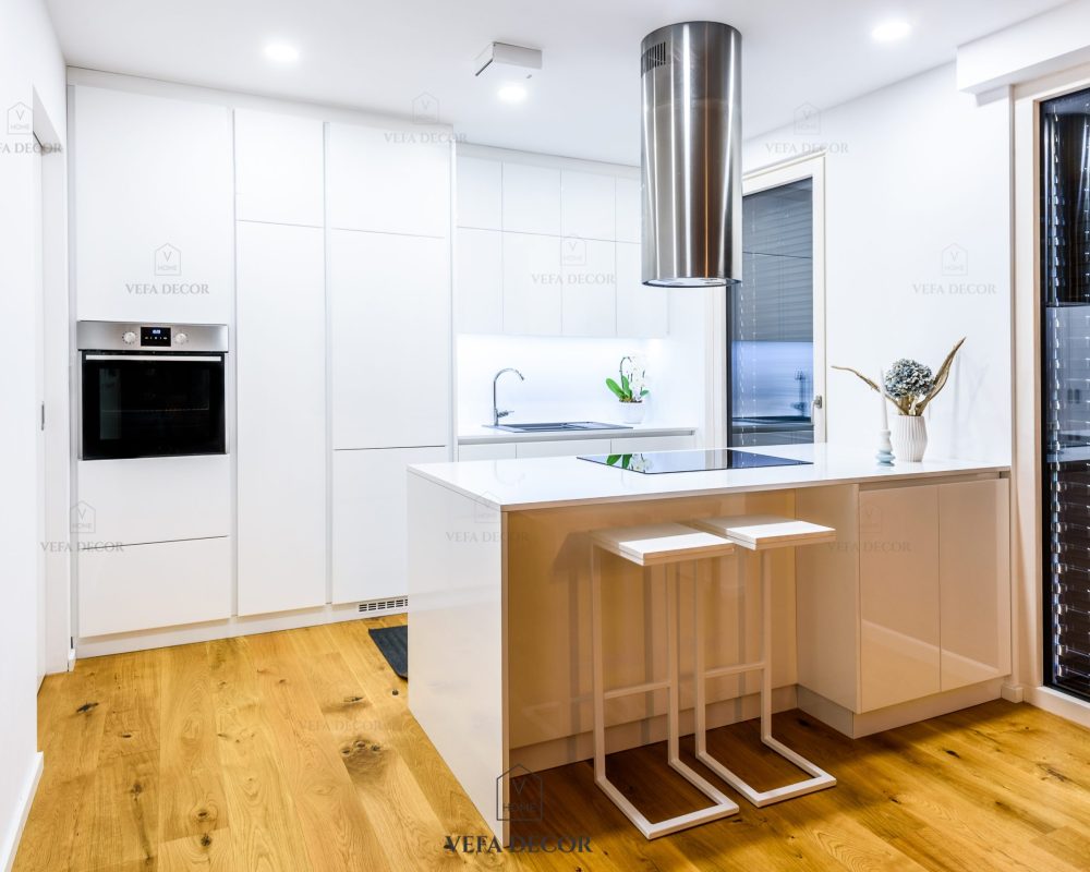 Interior design new modern white kitchen with kitchen appliances. Luxury residential kitchen with sink, stove, hob and white wooden cupboards and hard wood floor.